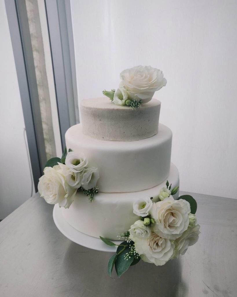 Gâteau de mariage vegan à deux étages, décoré de roses blanches et feuillage, idéal pour un mariage élégant et raffiné.