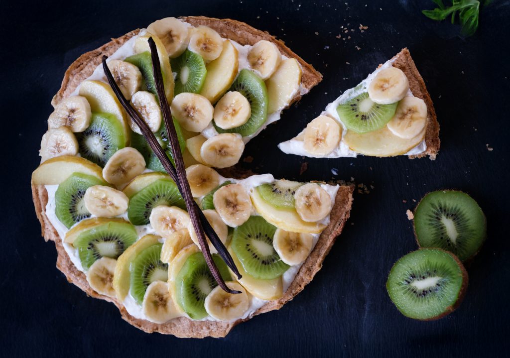 Tarte de saison vegan avec kiwis, bananes et pommes, décorée de gousses de vanille, idéale pour les desserts frais et gourmands. Disponible en format individuel ou à partager.